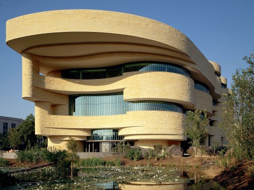 Exterior of light, natural stone building with undulating sides and curved windows.