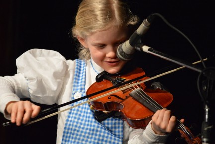 A young girl stands in front mic playing the violin.